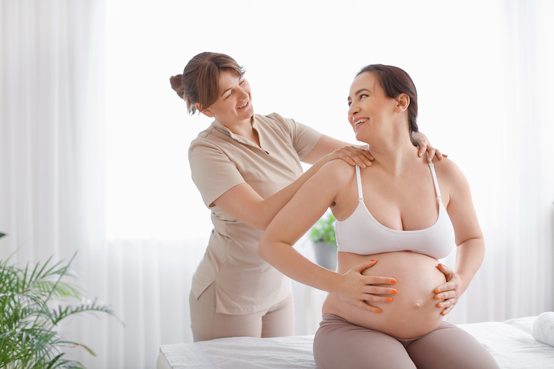 Pregnant woman getting prenatal massage by therapist on couch in spa salon