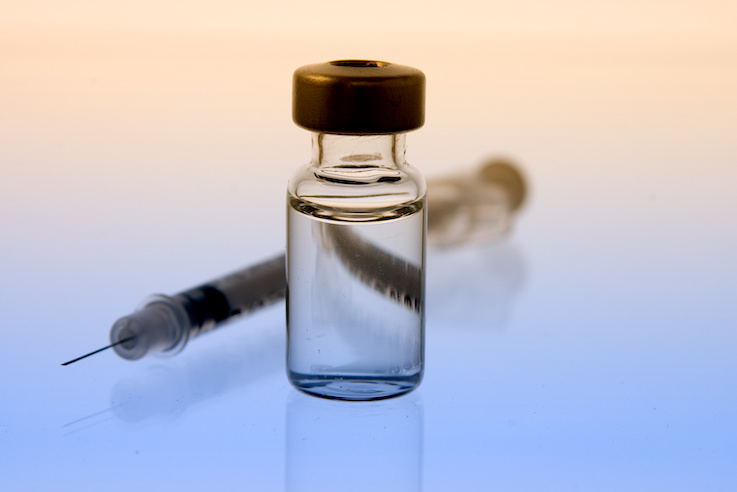 Syringe and vial on a baby blue and light orange background